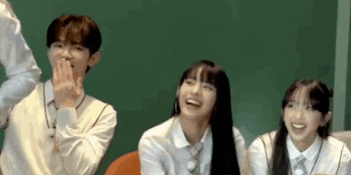 a group of people are sitting next to each other in front of a green board .