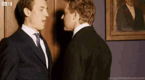 two men in suits and ties are standing next to each other and kissing in front of a painting .