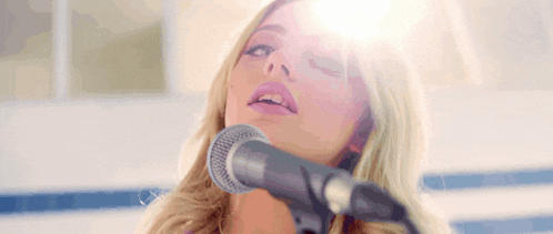 a woman is singing into a microphone with the sun shining through her eyes