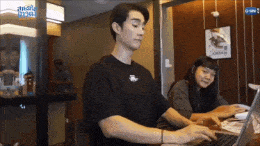 a man and a woman are sitting at a table using a laptop computer .