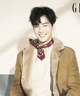 a young man wearing a fur coat and a bandana around his neck is smiling .