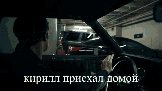 a man is driving a car in a parking garage with russian writing on the side