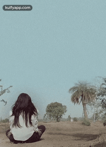 a woman is sitting on the ground in a field looking at trees .