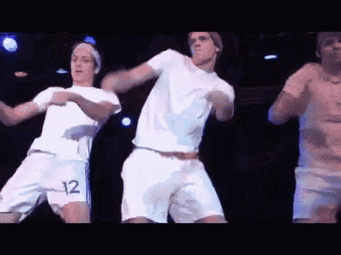 three men in white shirts and shorts are dancing on a stage . one has the number 12 on his shorts .