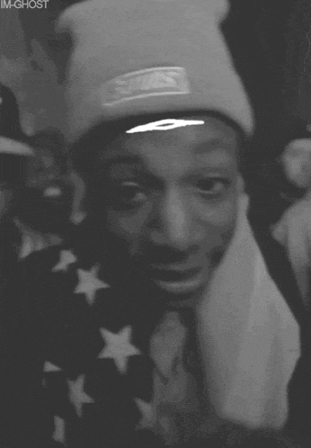 a black and white photo of a man wearing a beanie with a white eye on his forehead