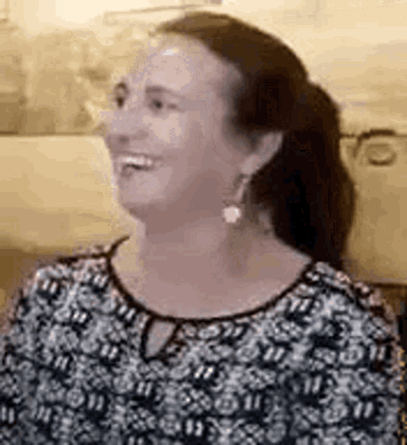 a woman wearing a black and white shirt and earrings is smiling and laughing .