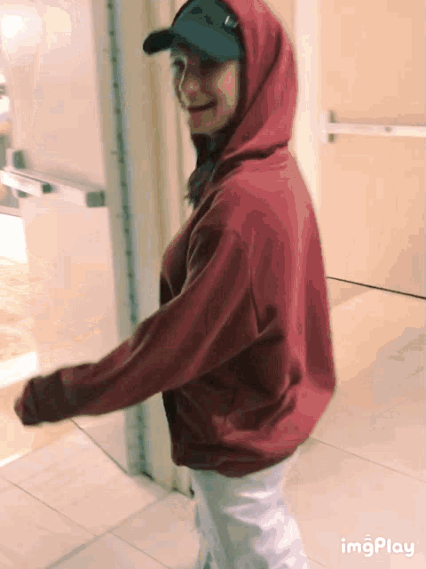 a woman wearing a red hoodie and a baseball cap is walking through a doorway