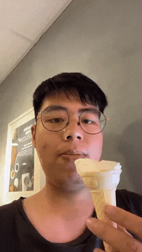 a man with glasses is eating an ice cream cone in front of a sign that says ' ice cream ' on it