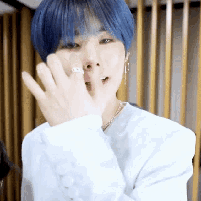 a young man with blue hair and a ring on his finger is covering his face .
