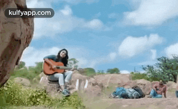 a woman is sitting on a rock playing a guitar in the woods .
