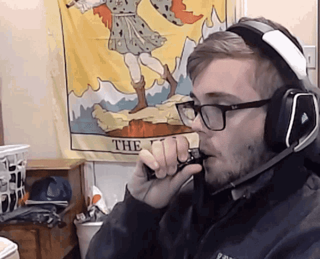 a man wearing headphones and glasses is smoking a cigarette in front of a tarot card that says the fool
