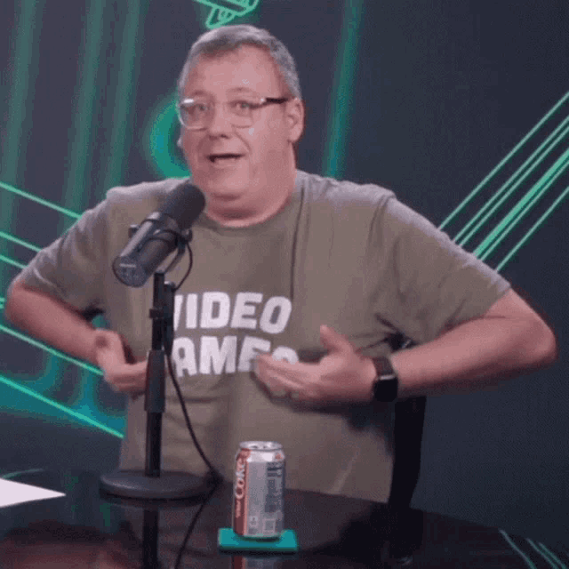 a man wearing a video game t-shirt is talking into a microphone