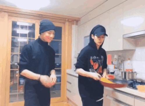 two men are cooking in a kitchen and one of them is wearing a black hoodie with a skull on it