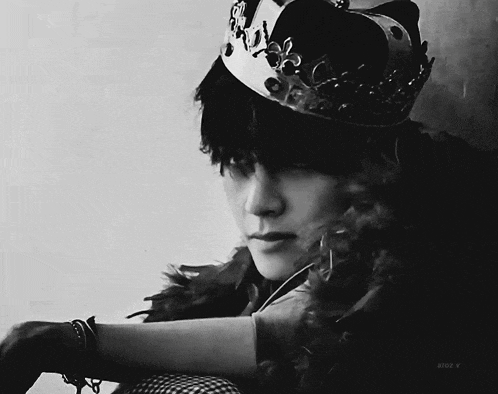 a black and white photo of a person wearing a crown and a feather boa