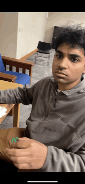 a man in a grey sweater is sitting at a table holding a piece of paper with the letter m on it
