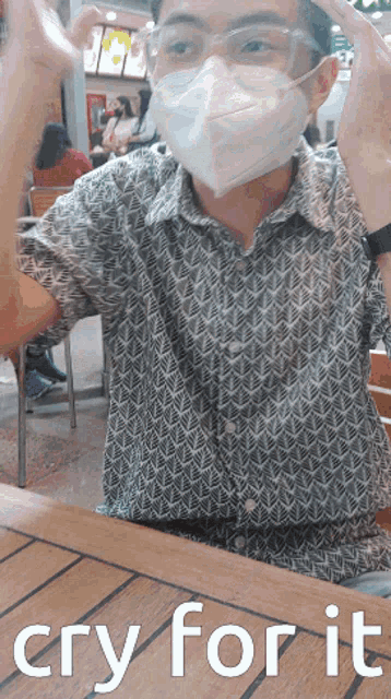 a man wearing a face mask is sitting at a table with the words cry for it above him