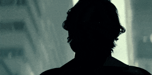 a silhouette of a man 's back is shown in a dark room
