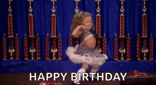 a little girl in a tutu is dancing on a stage in front of trophies and the words `` happy birthday '' .