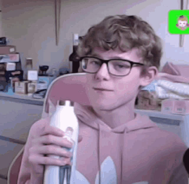 a young man wearing glasses and a pink hoodie is holding a bottle .