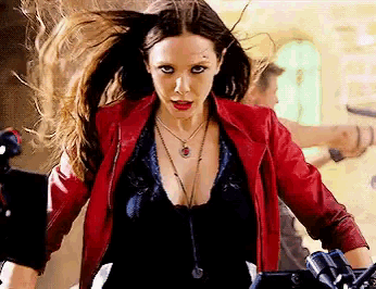 a woman wearing a red jacket and a black top is standing in front of a camera .