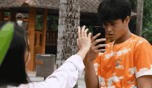a man wearing an orange shirt with the letter g on it looks at his phone