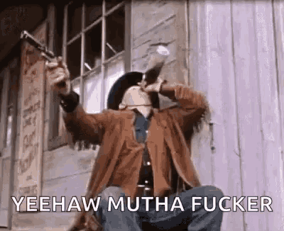 a cowboy is sitting in front of a building holding a gun .