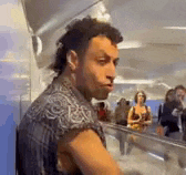 a man with a mullet is standing in front of a crowd of people in an airport .