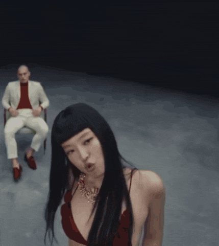 a woman in a red bikini is holding her hair while a man sits in a chair behind her