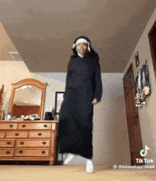 a person in a black dress is dancing in a room with a dresser and a mirror