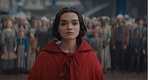 a woman wearing a red cape is standing in front of a crowd