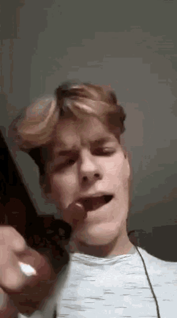 a young man is sticking his tongue out while holding a red object in his mouth .
