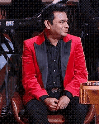 a man in a red jacket and black shirt is sitting in front of a korg keyboard