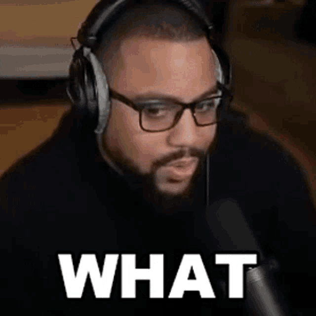 a man wearing headphones and glasses is sitting in front of a microphone with the word what written on the screen .