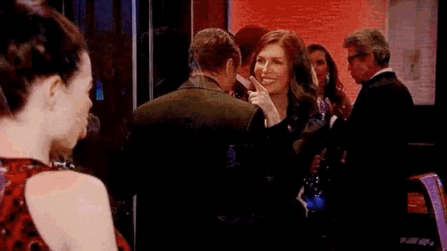 a man and a woman are standing next to each other in a room and the woman is pointing at the man 's face .