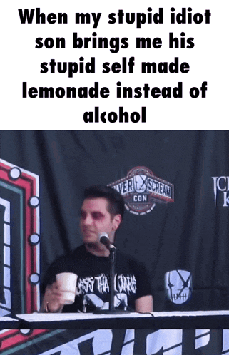 a man sitting at a table with a cup of lemonade in front of a microphone