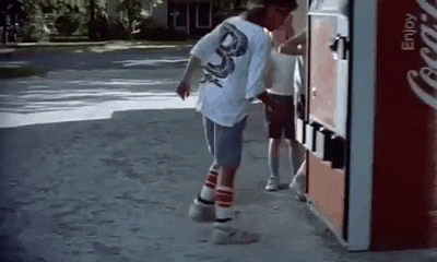 a man is standing next to a coca cola vending machine on the sidewalk .