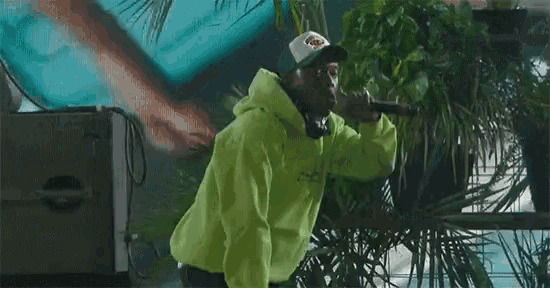 a man in a neon green hoodie is singing into a microphone while wearing headphones