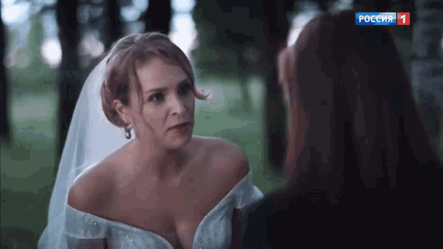 a woman in a bride 's dress is talking to another woman with the number 1 on the bottom right corner