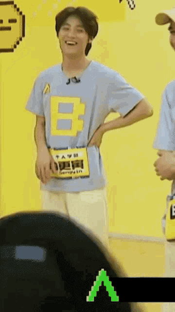 a man in a blue t-shirt with a yellow b on it is standing in front of a yellow wall .