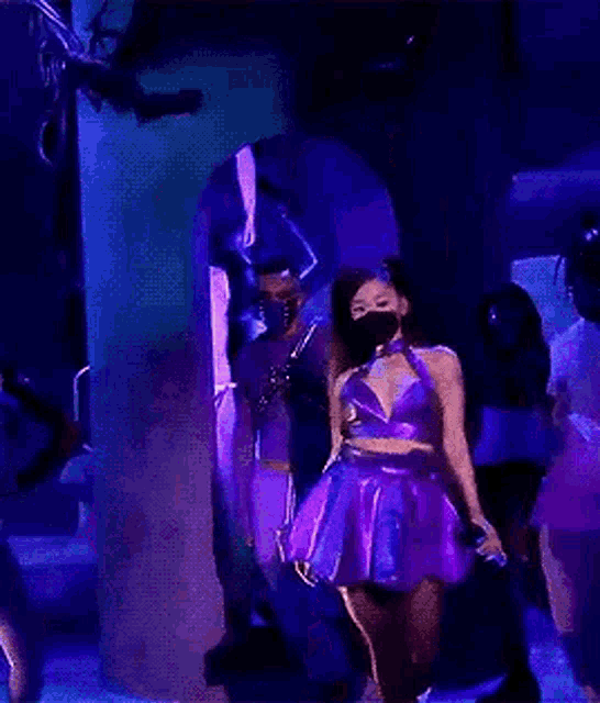 a woman in a purple dress is wearing a mask and holding a microphone .
