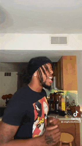 a man wearing a black t-shirt with a picture of mickey mouse on it is standing in a kitchen