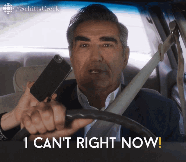 a man in a car holding a cell phone with the words i can 't right now below him