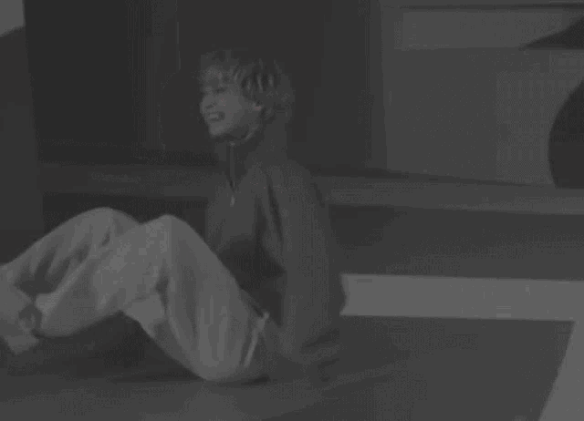 a young boy is sitting on the floor with his arms outstretched in a black and white photo .