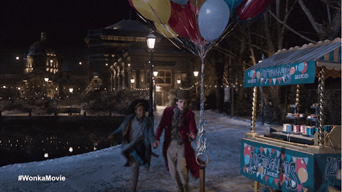 a man holding a bunch of balloons in front of a candy cart that says wonka 's