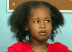 a little girl with curly hair wearing a red shirt is making a funny face .