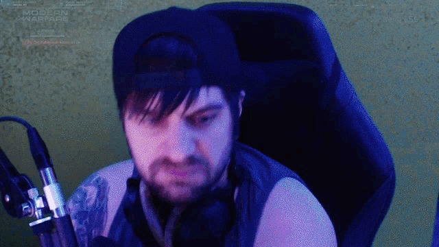 a man wearing a hat and headphones is sitting in front of a screen that says modern warfare