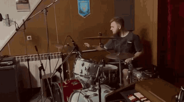 a man is playing drums in a room with a banner on the wall that says ' a ' on it .