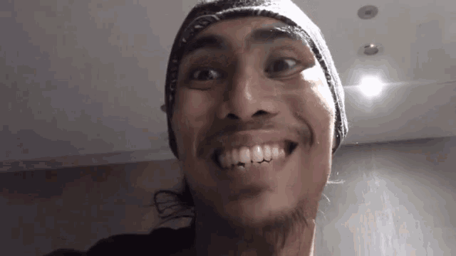 a man with a beard wearing a bandana and a hat is smiling .