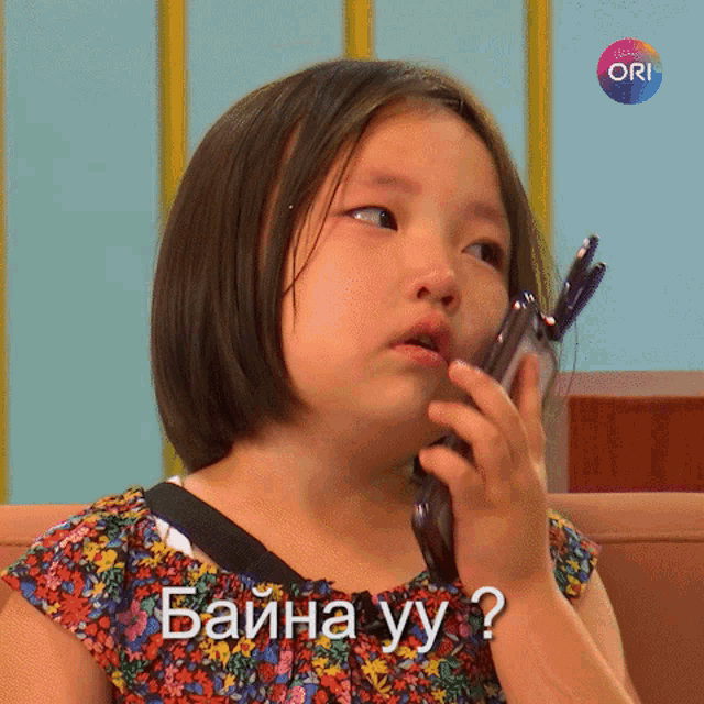 a little girl talking on a cell phone with the word ori on the bottom left