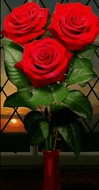 three red roses in a red vase with green leaves